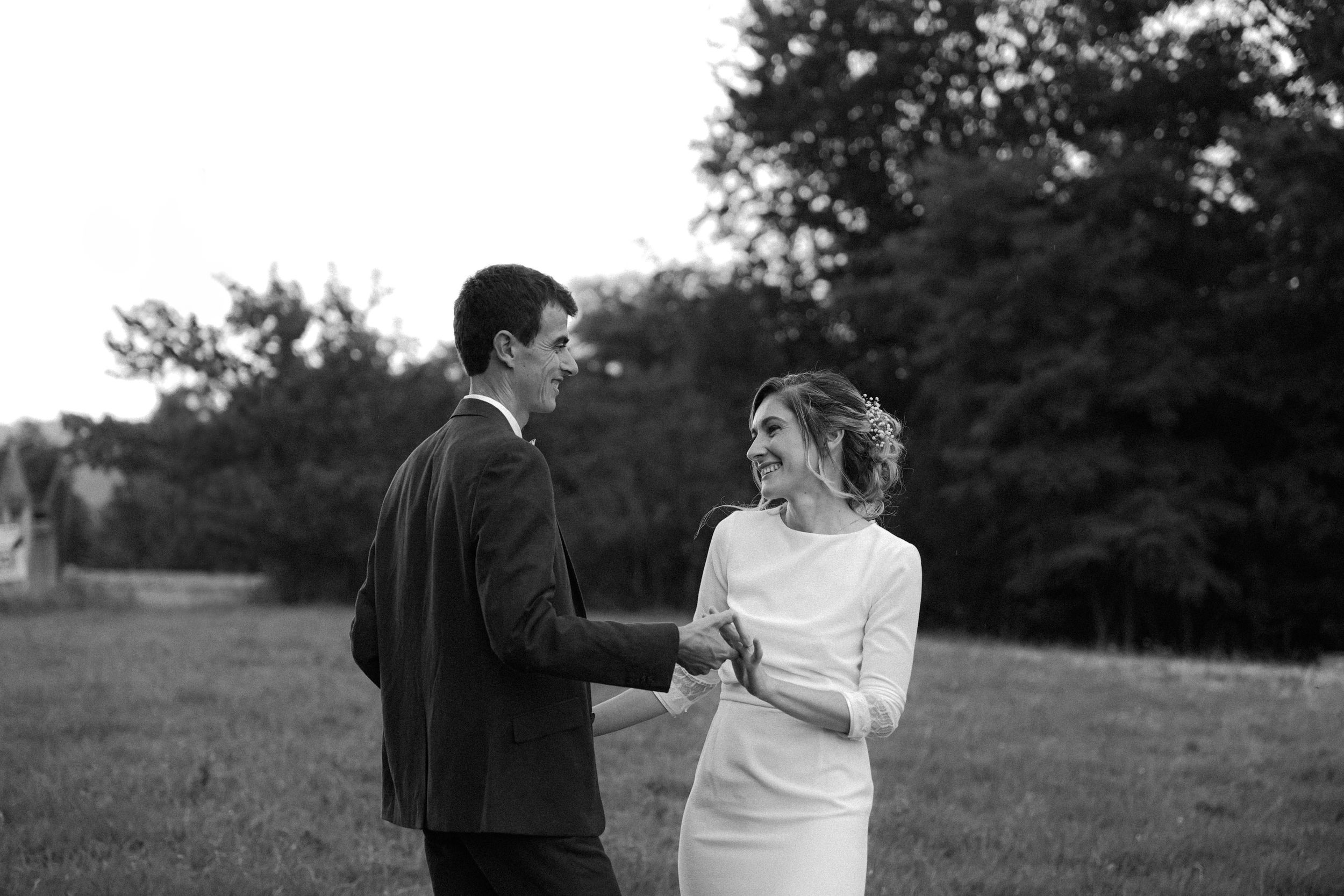 Black and white photo of newlyweds holding hands and smiling in an outdoor garden setting.