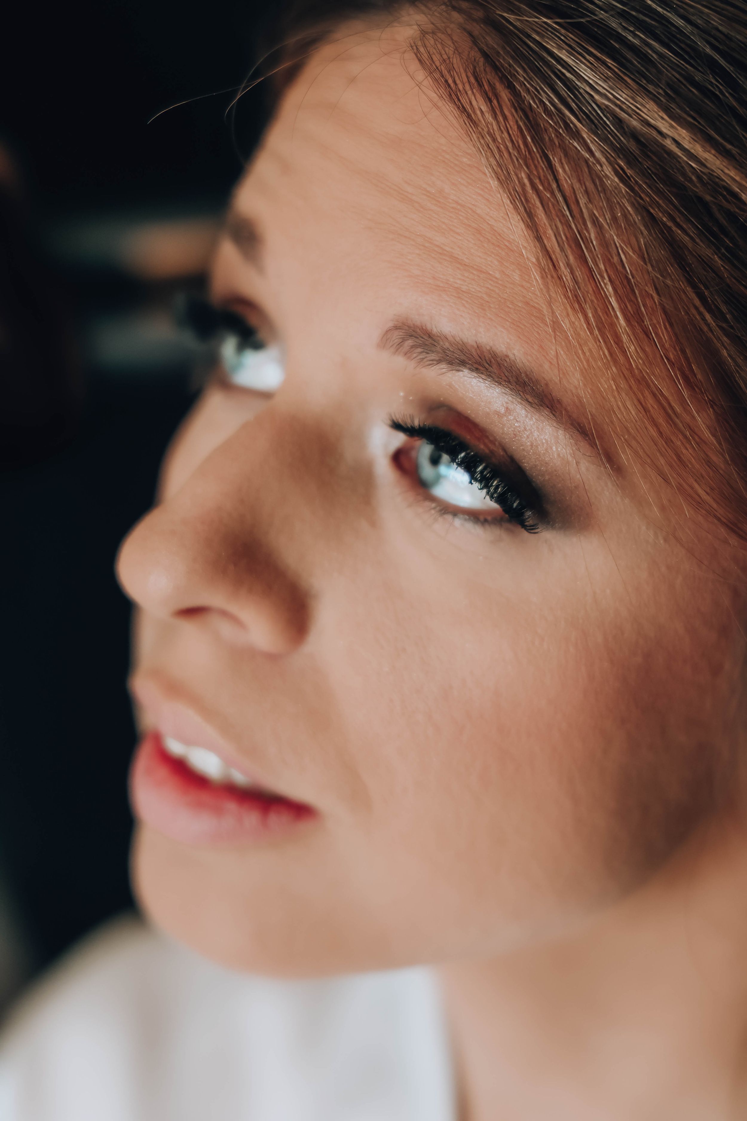 Close-up portrait of a woman with blue eyes, smoky eye makeup, and natural skin, gazing upward in soft light.