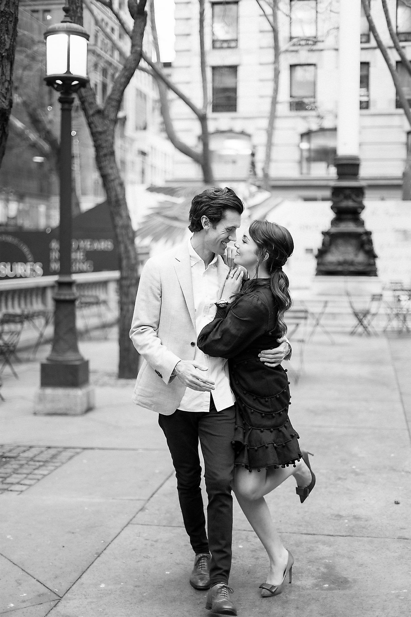Romantic couple sharing an intimate moment on a city street with vintage lampposts and buildings in the background.