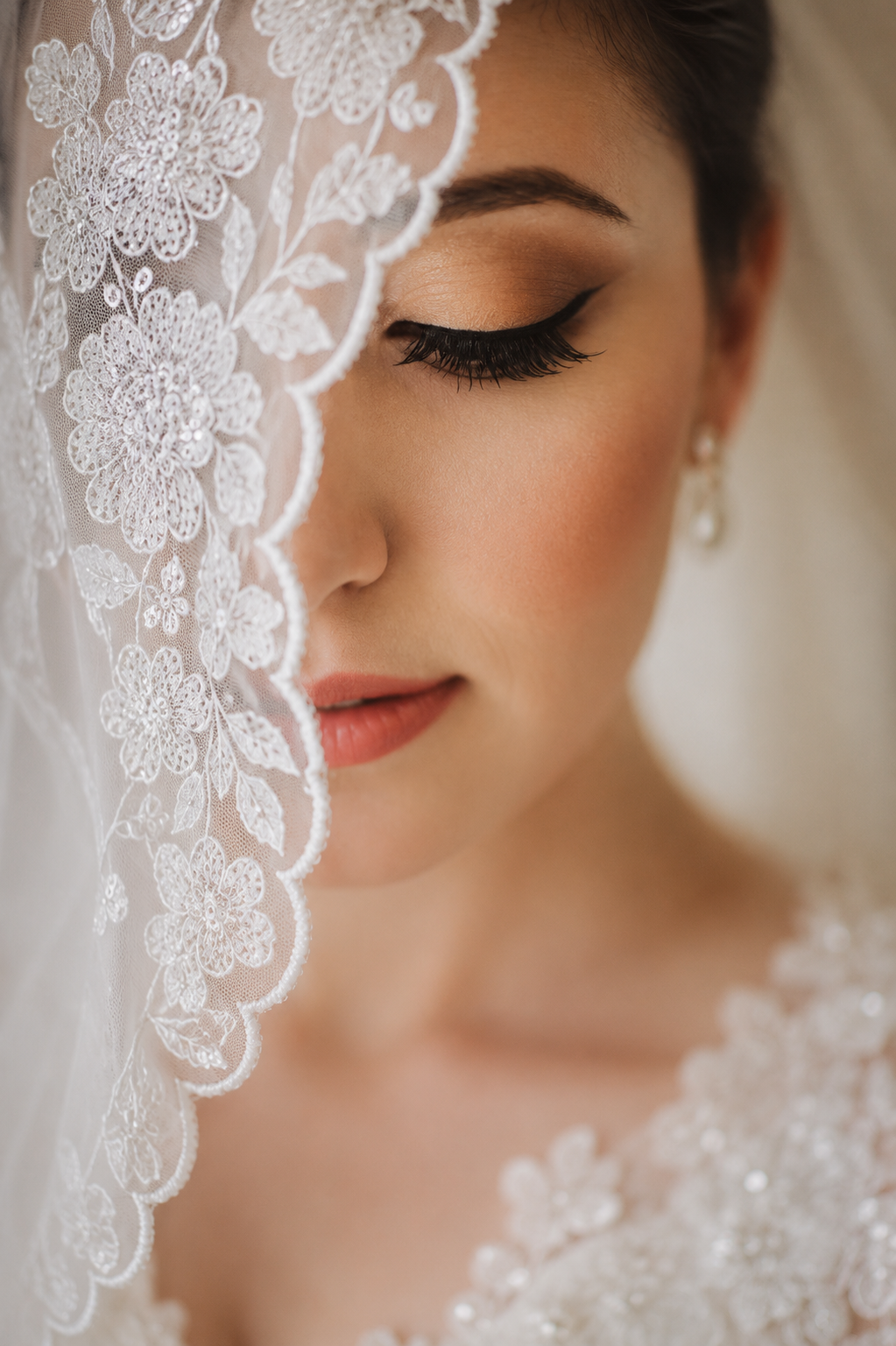 Artistic close-up of a bride with warm glam makeup, lashes, and intricate lace veil draped over her face.