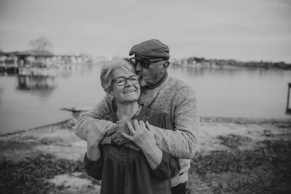 A loving couple embraces by the waterfront in black and white as they share a tender moment near a marina.