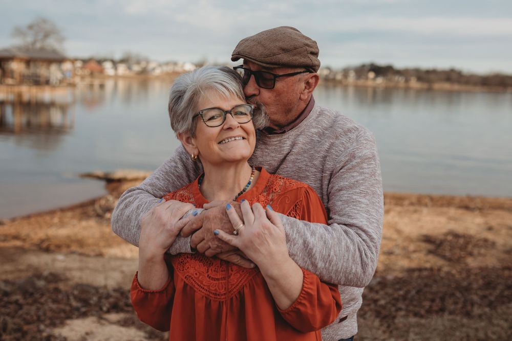Affectionate senior couple embracing on a lakeside beach during sunset in autumn.
