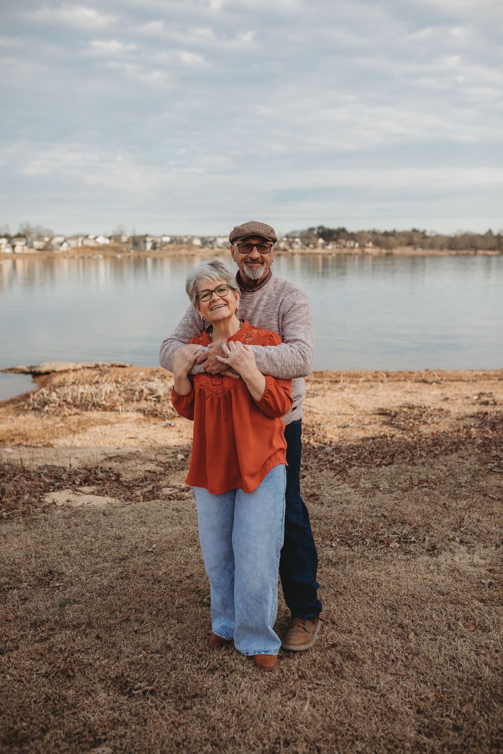 Couple in casual attire sharing a tender moment by a serene lakeside on an overcast day.