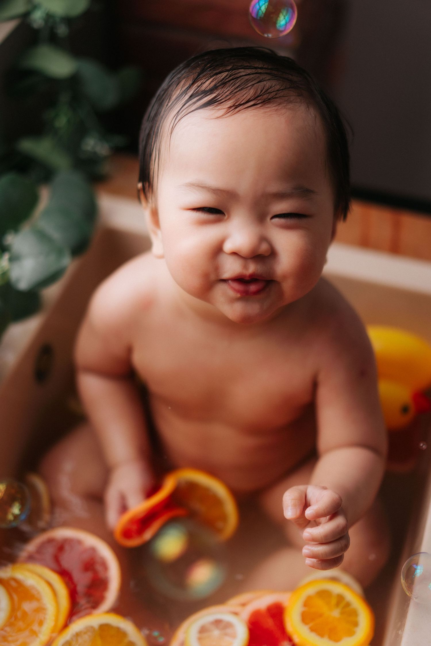 A baby lies on their tummy next to bright orange citrus slices during a colorful photo session.