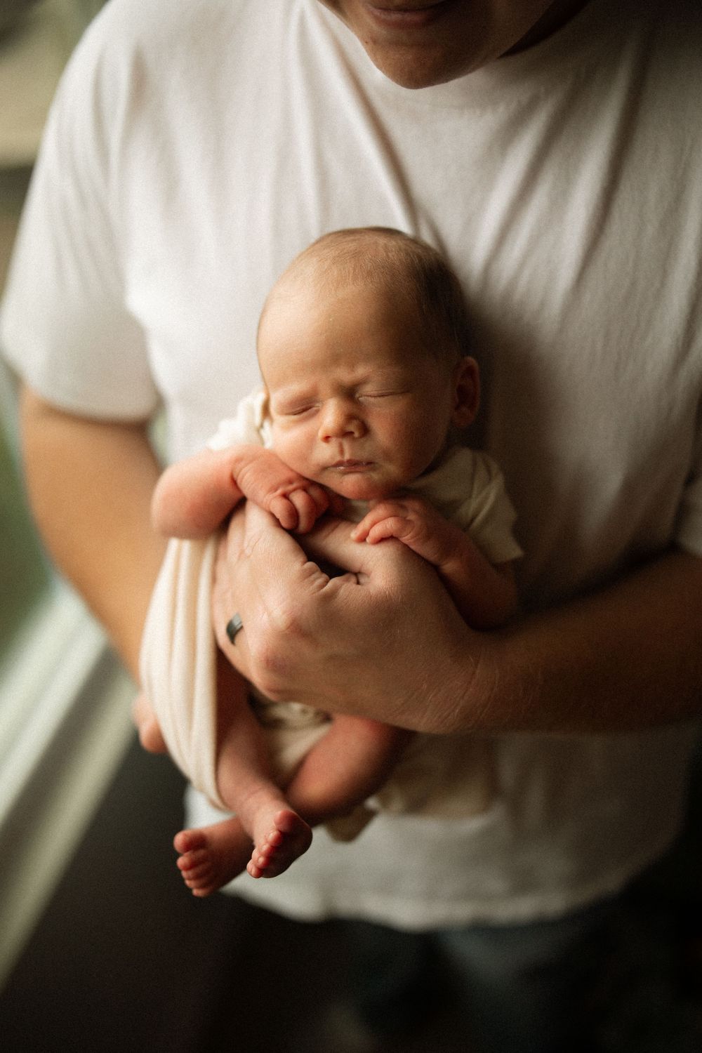 A series of images showing a sleeping newborn baby being gently cradled in someone's arms wearing a white shirt.