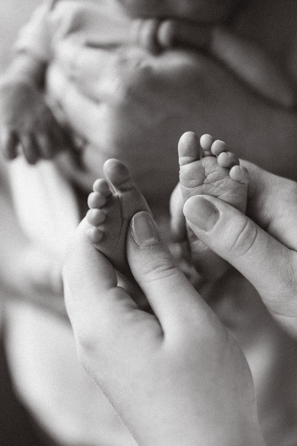 Close-up black and white photo of tiny baby toes and feet being gently held by adult hands.