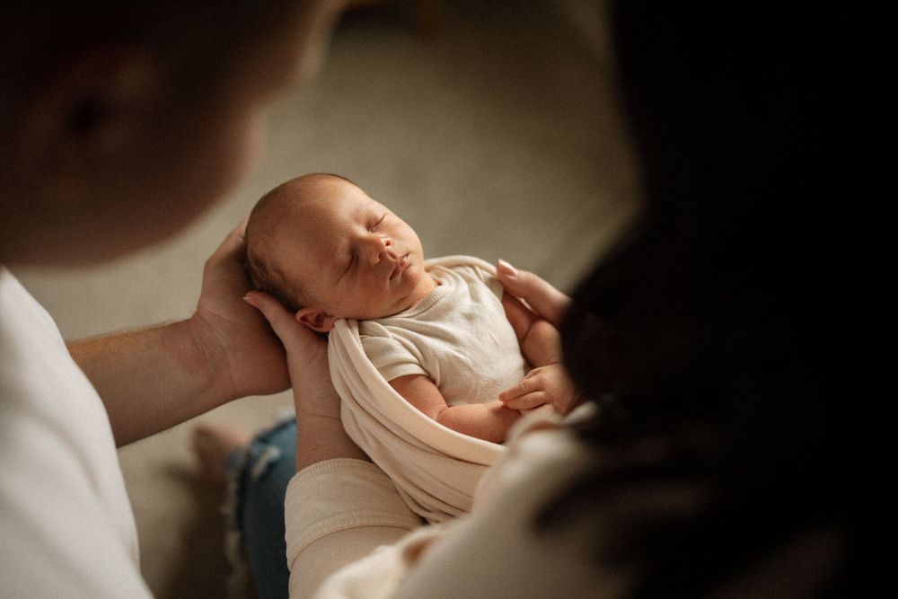 A series of intimate close-up shots showing hands tenderly cradling a sleeping newborn baby in soft light.