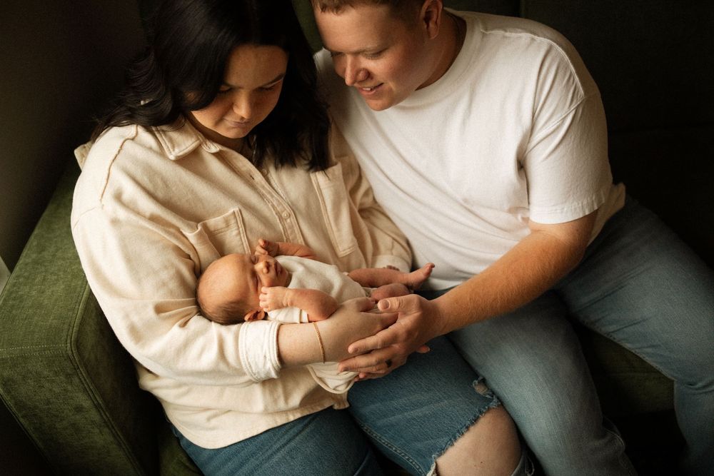 Parents sitting on green couch tenderly holding and looking at their newborn baby in intimate home setting.