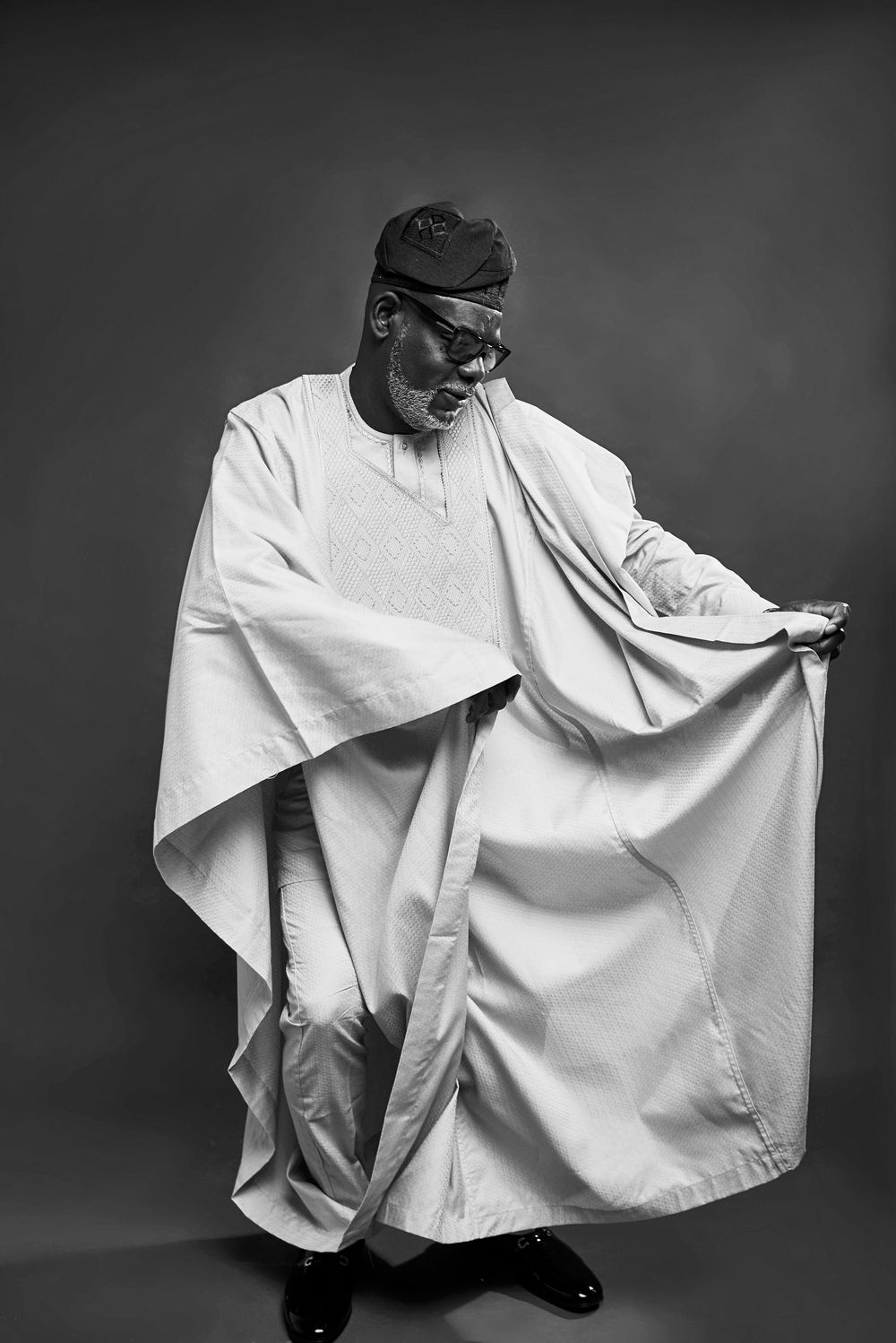 A dramatic black and white photo sequence shows a figure in white agbada fabric performing flowing dance movements.