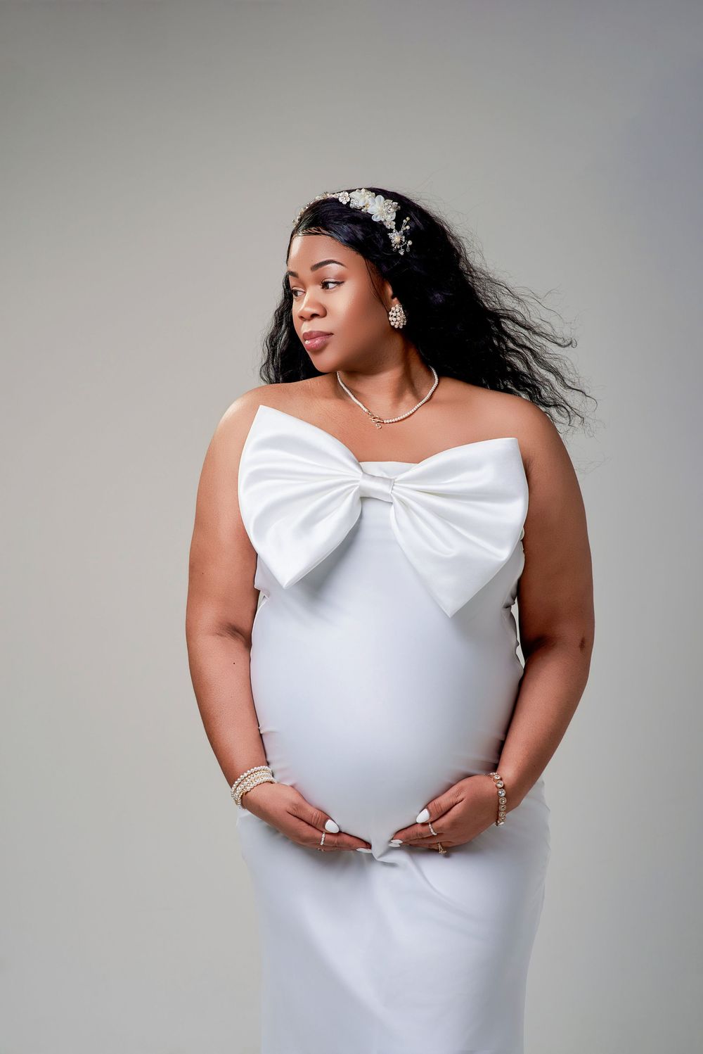 A stunning maternity portrait featuring a white strapless gown with large bow detail and delicate hair accessories.