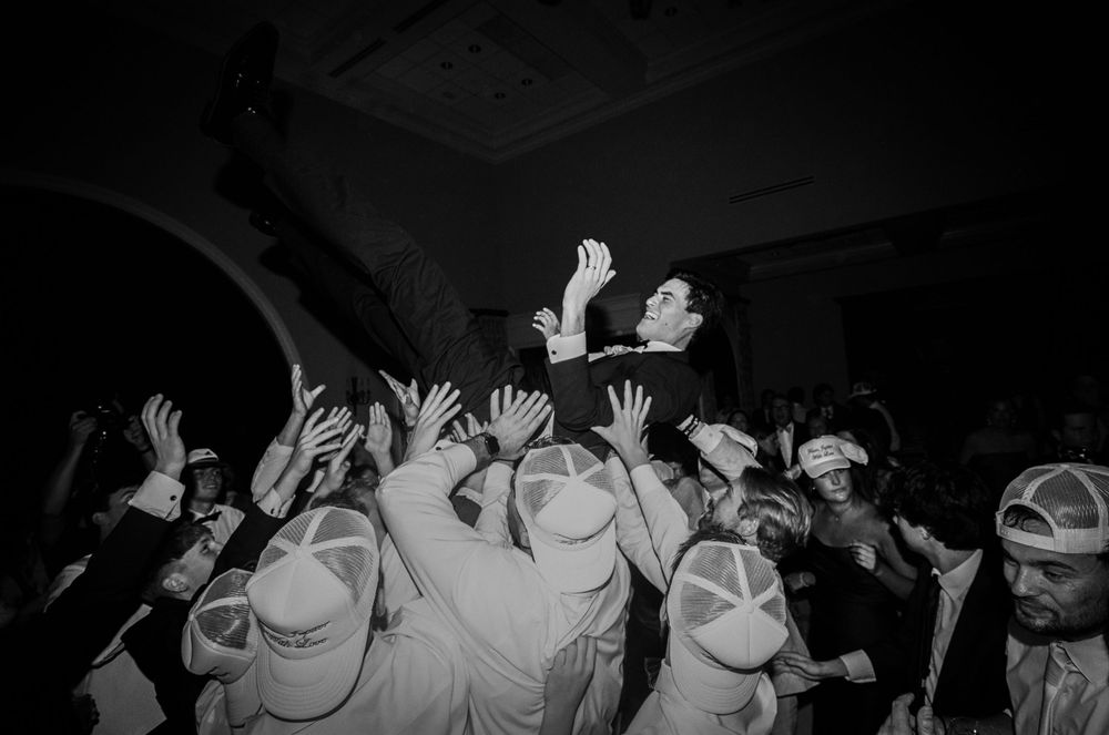 A black and white photo of wedding guests raising their hands during a reception celebration.