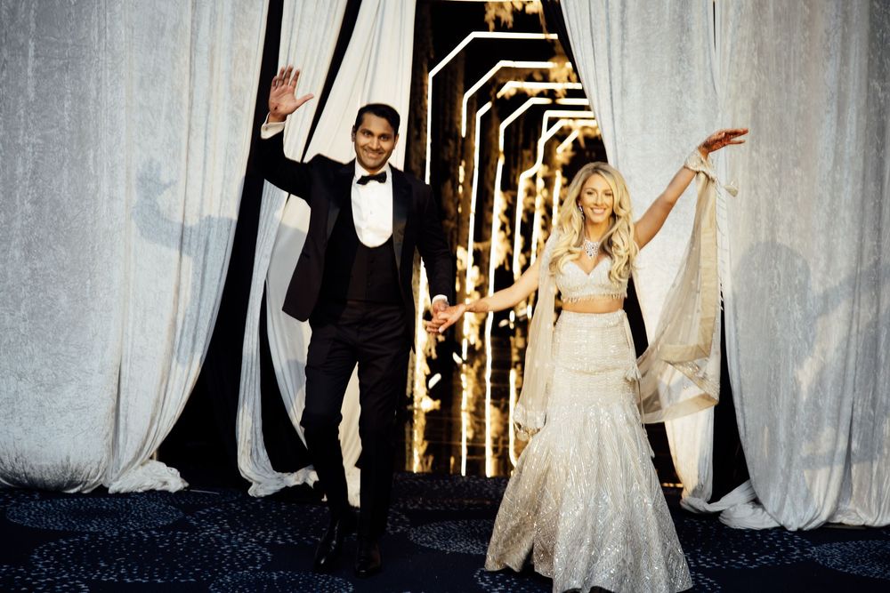 A wedding couple dances together during their first dance in an elegant ballroom with white drapery and warm lighting.