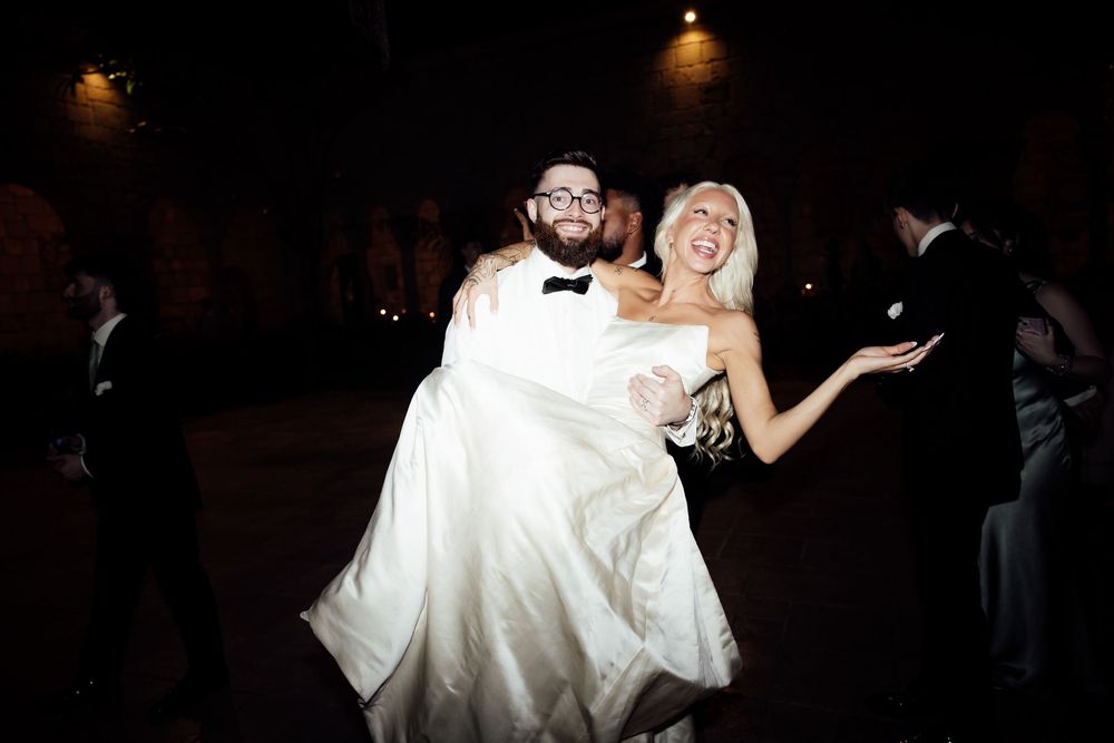 A couple dances together at their wedding reception in a dark ballroom with dramatic lighting.