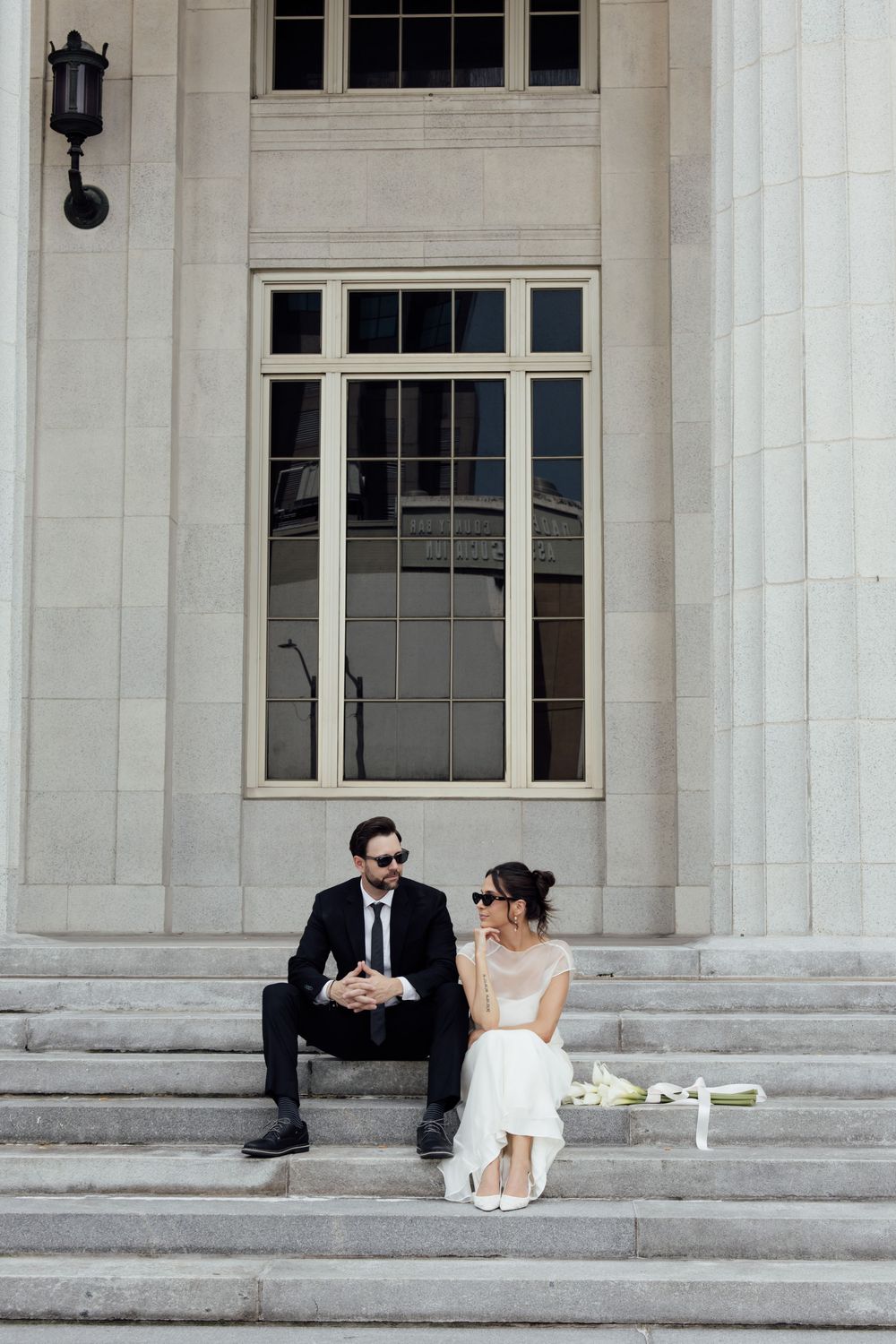 A couple sits together on grand stone steps of a classic building with white columns.
