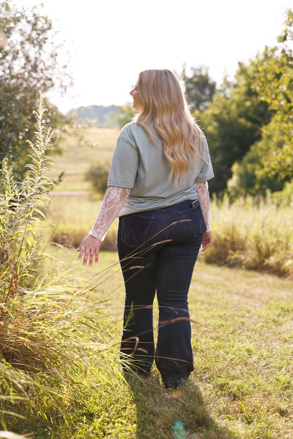 Back view of person in casual attire standing in tall grass during golden hour.
