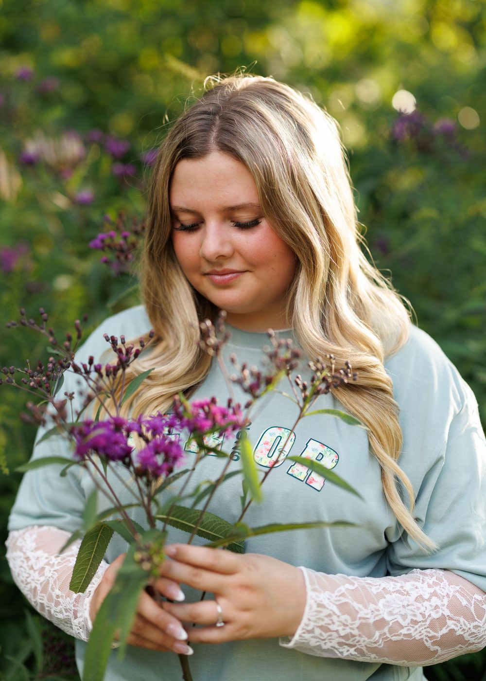 Person in mint sweater with lace sleeves holding purple wildflowers in garden setting.
