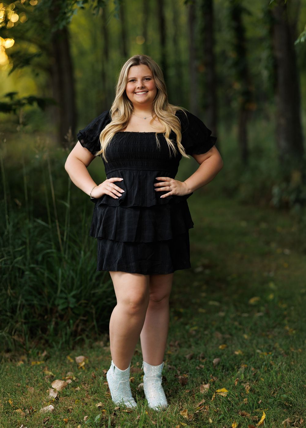 Outdoor portrait in black ruffle dress and white socks against forest background.