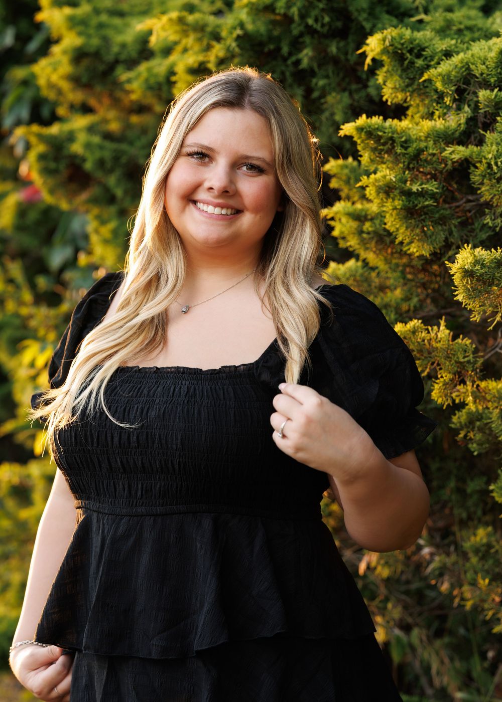 Outdoor portrait against yellow flowering bush in black summer dress.