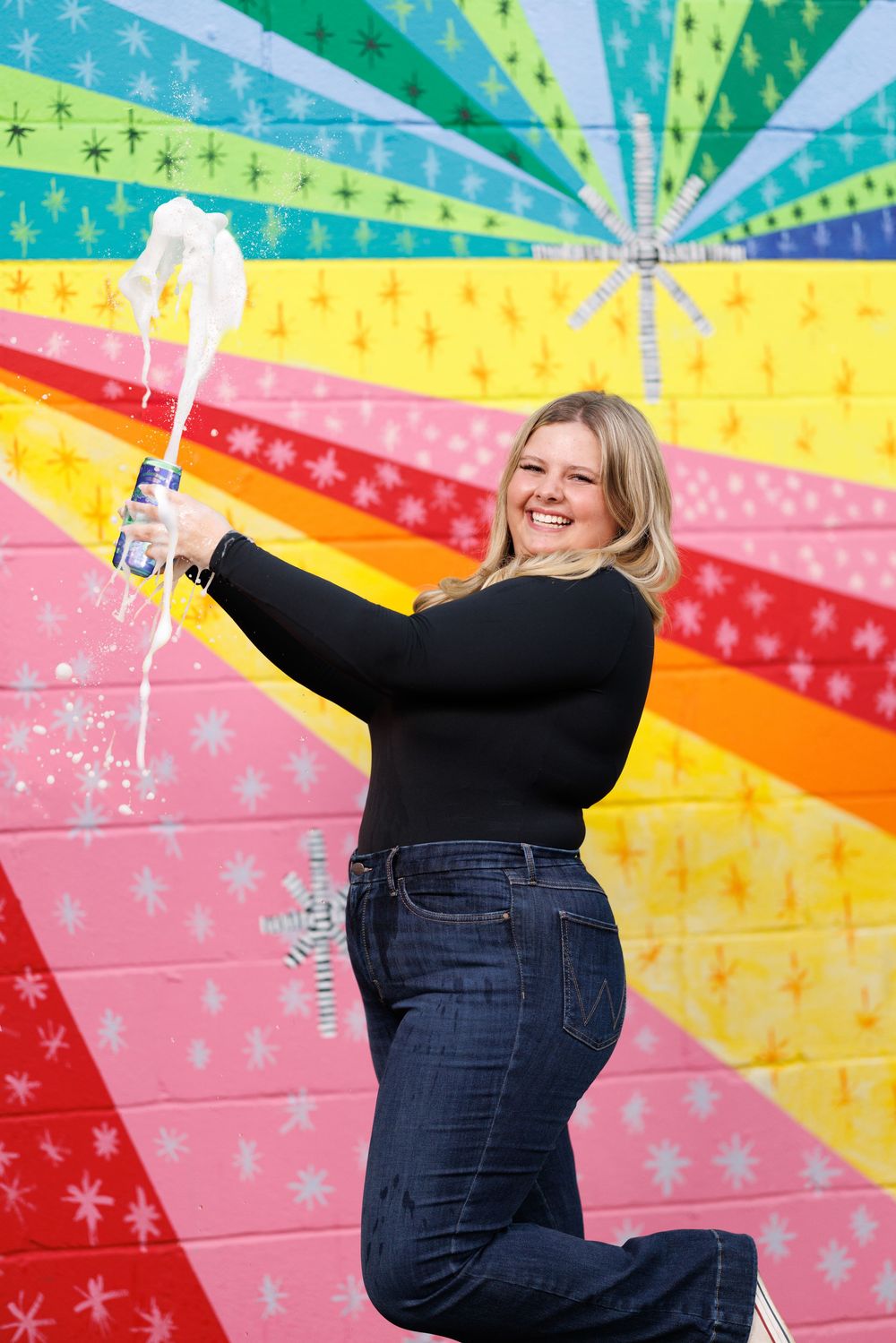 Energetic poses against a vibrant rainbow-colored wall with stars and stripes pattern.