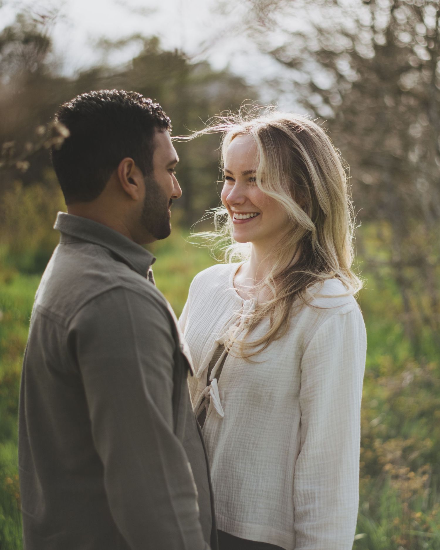 A couple shares a joyful moment together outdoors in a natural setting with soft lighting and greenery in the background.
