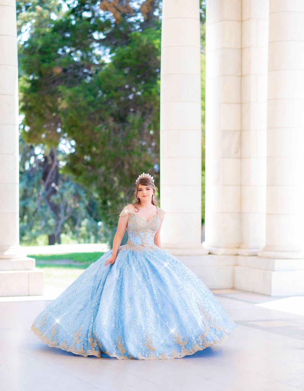 Dreamy princess photoshoot in blue ballgown among classical white pillars.