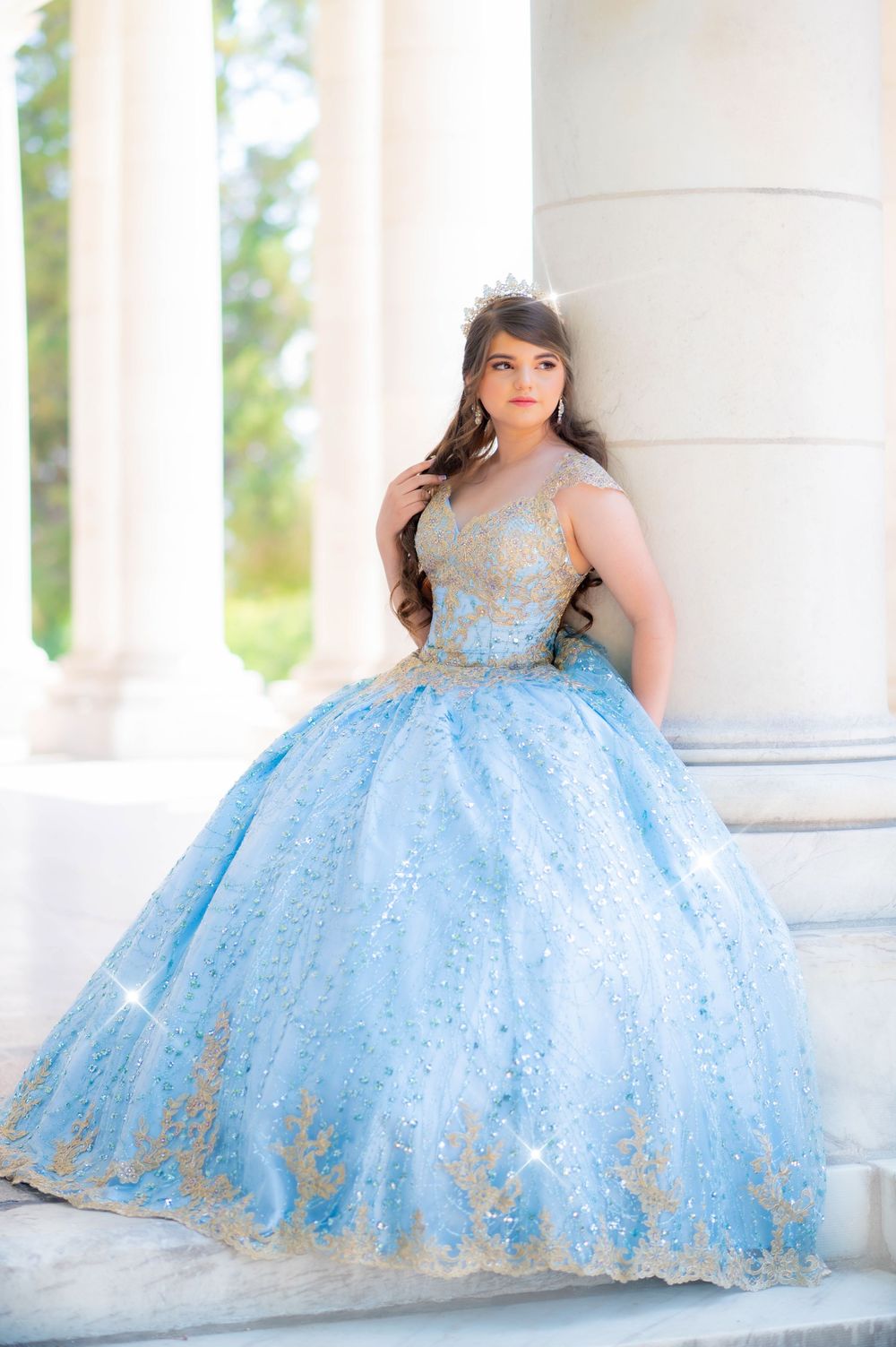 Flowing light blue ballgown with gold accents photographed between white columns.