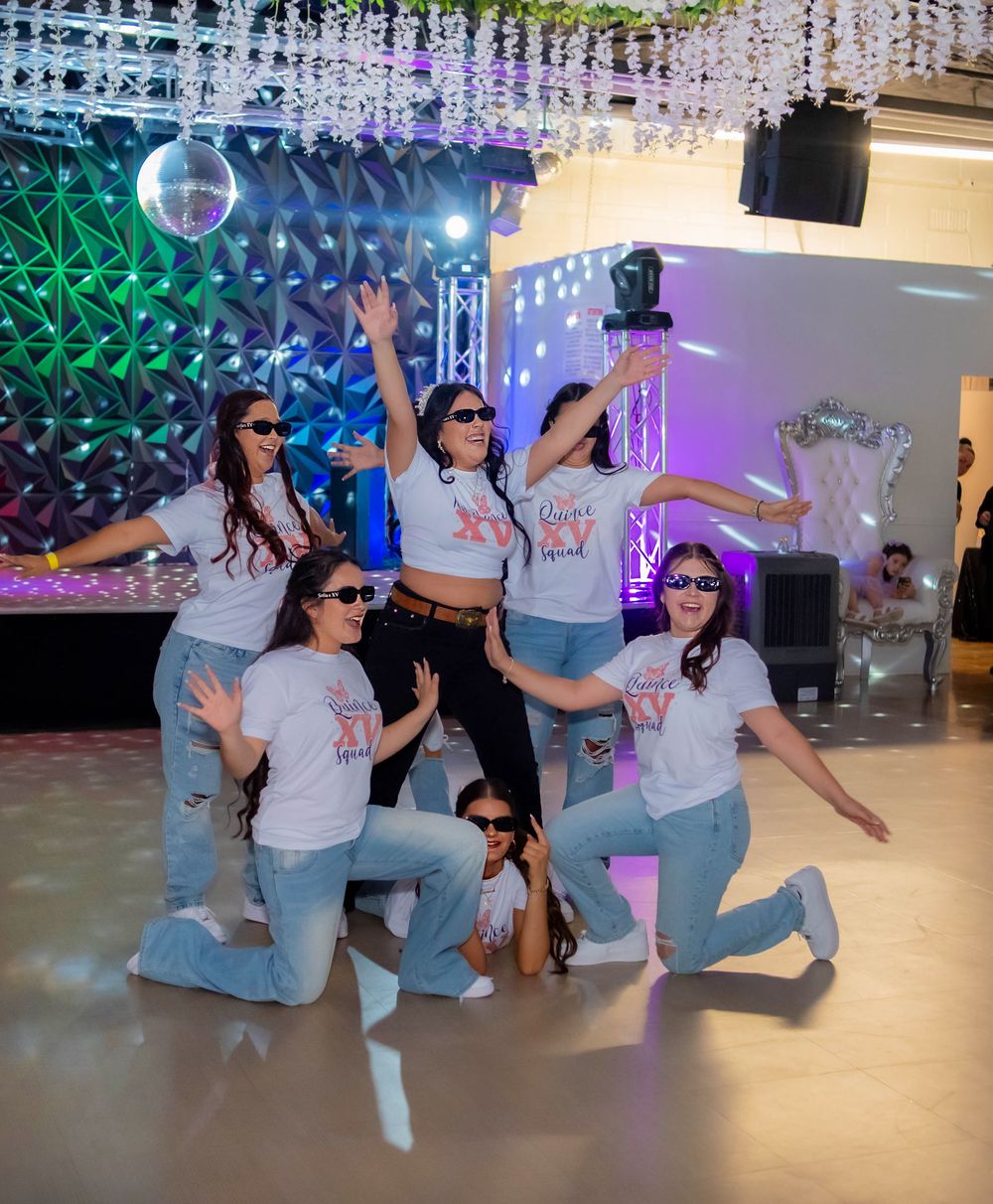 A choreographed dance group poses in matching outfits under party lighting.