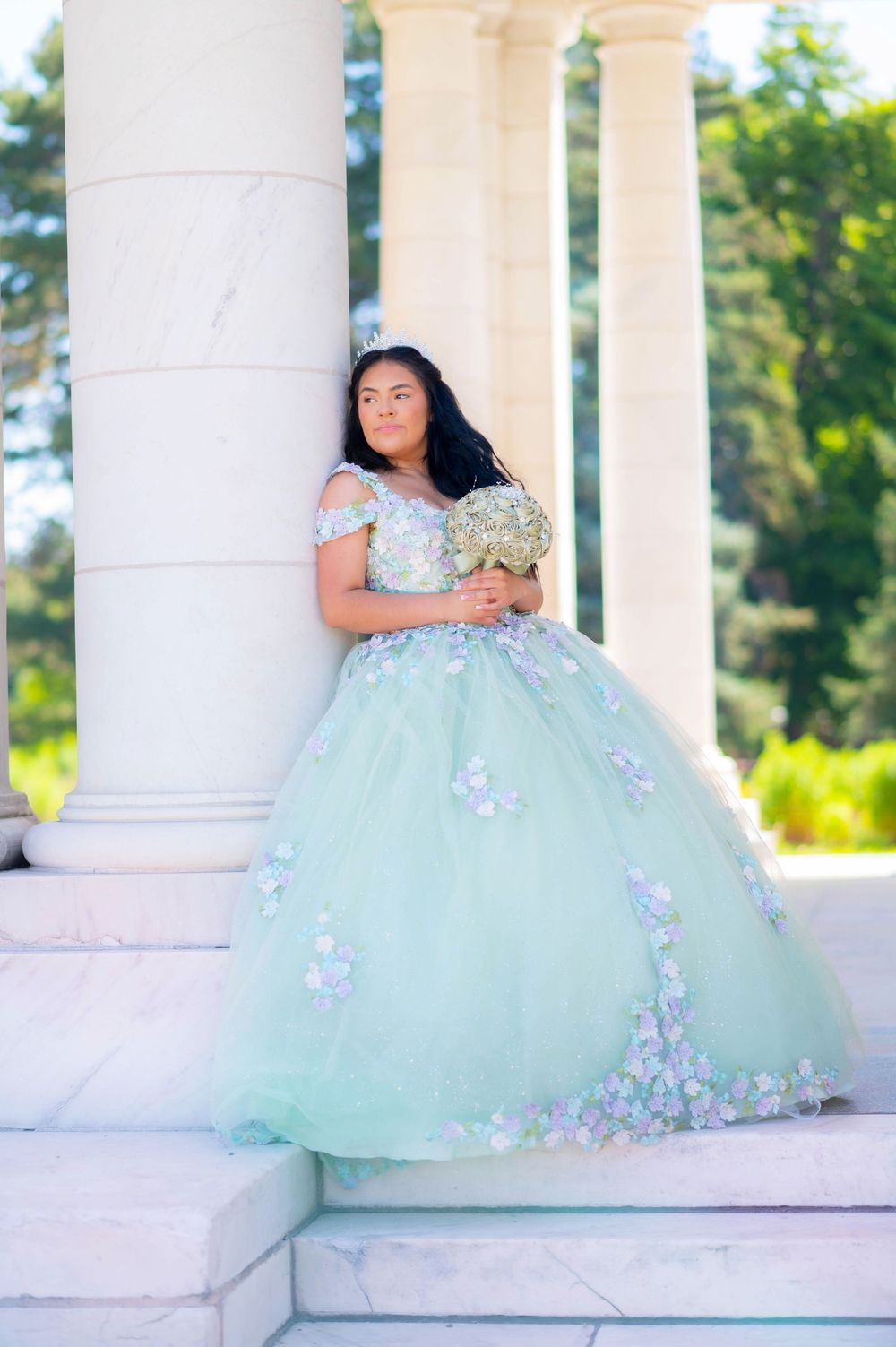 A mint green ball gown with floral details photographed against white classical columns.
