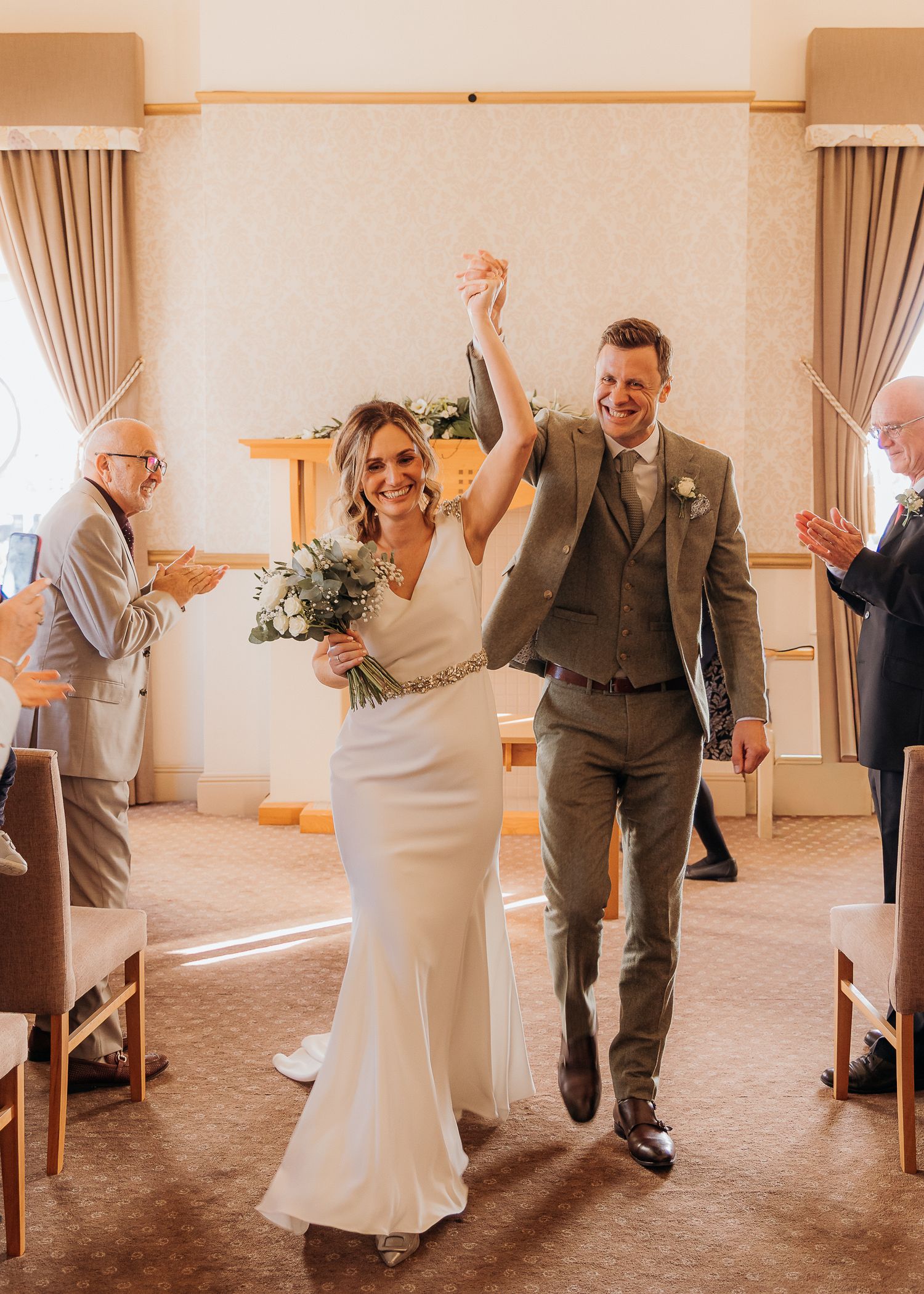 Couple dances and twirls in a bright reception hall with white chair covers.