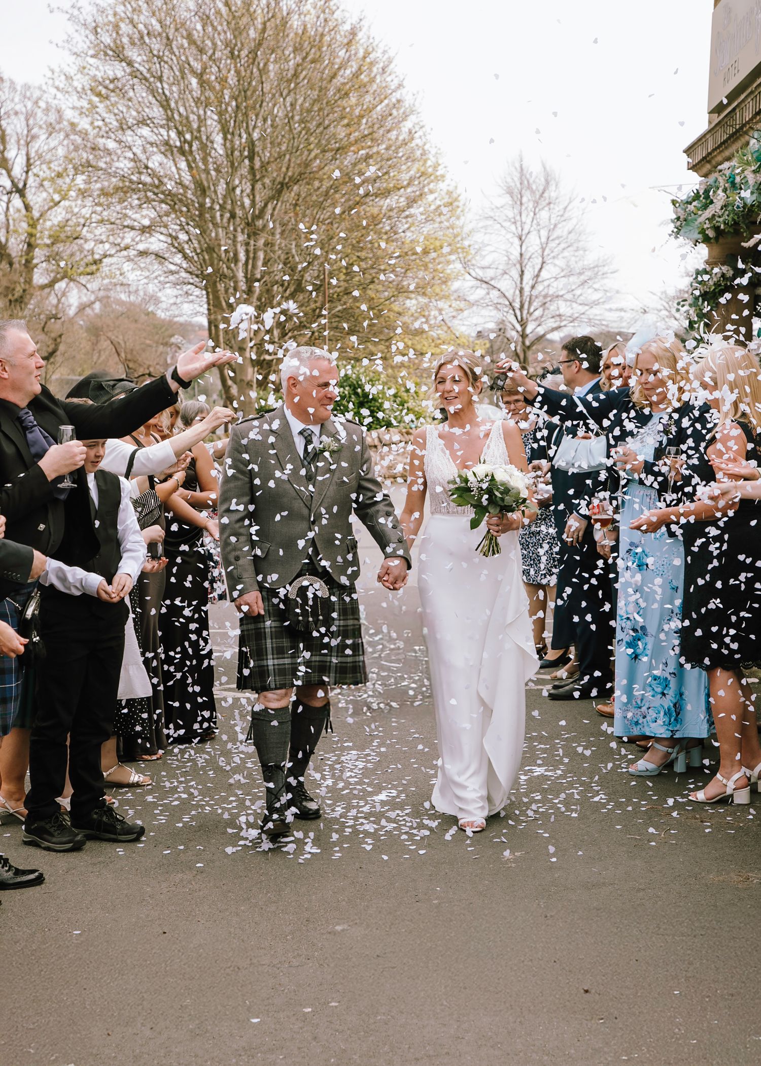 Wedding party walks through a shower of white confetti on a cloudy day.