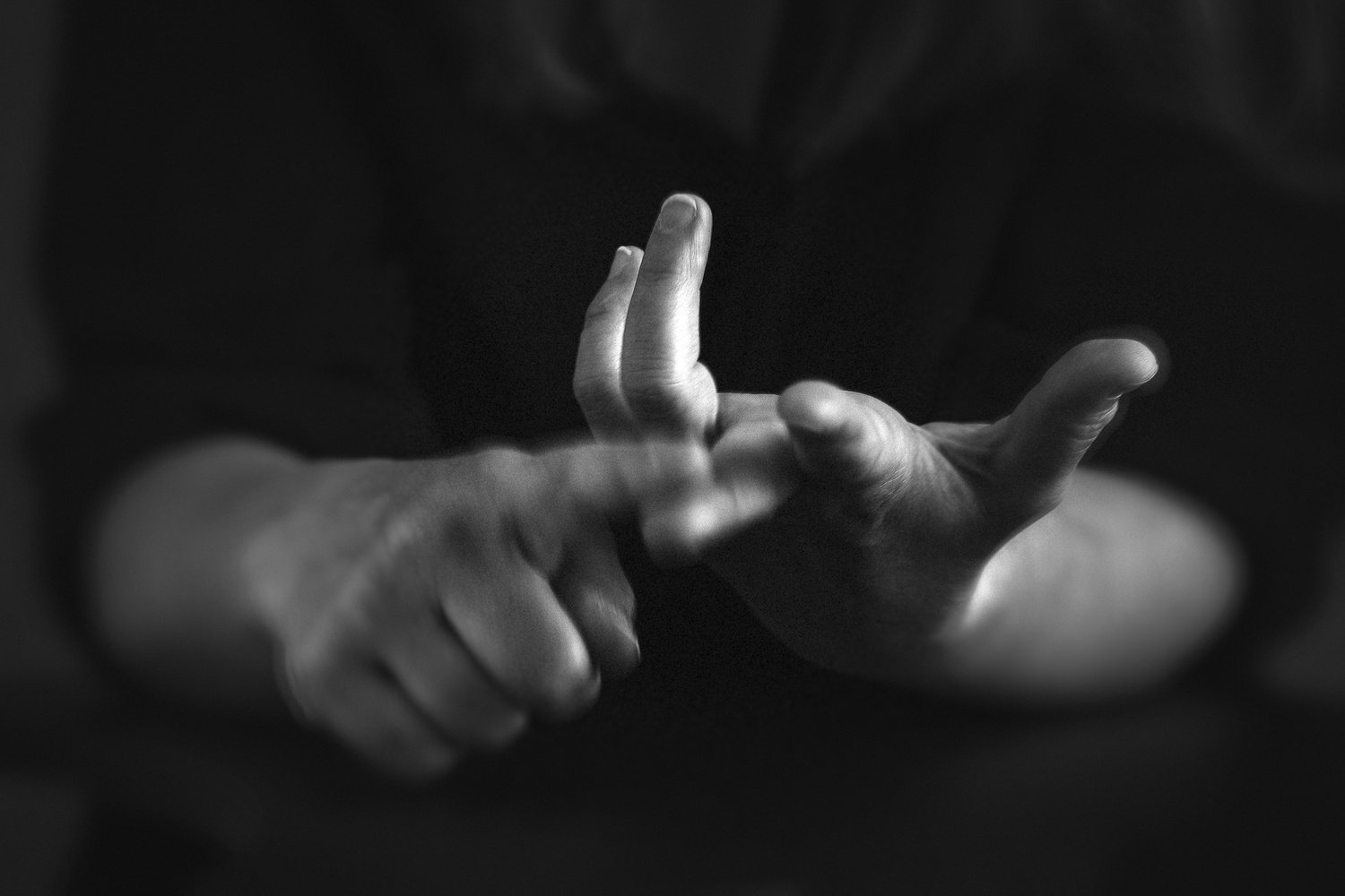Black and white close-up photograph of hands making expressive gestures against a dark background.