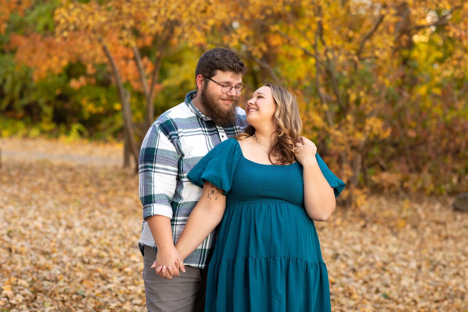 Engagement session of a couple looking into each other's eyes surrounded by fall colors in Iowa.