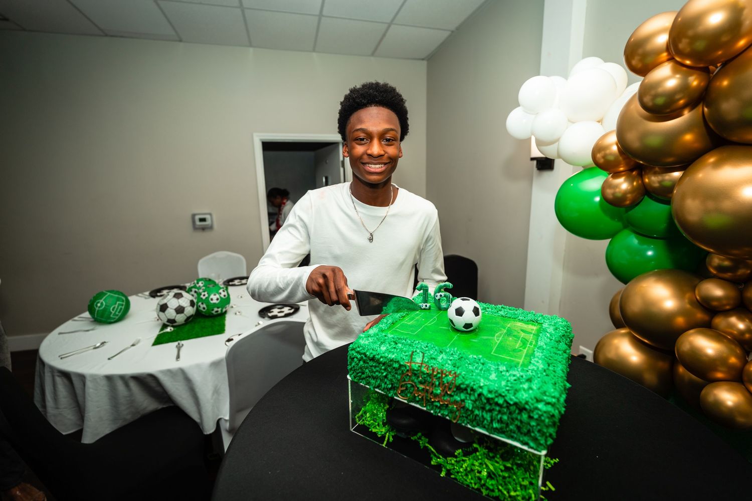A festive party setup with green and gold balloons, soccer-themed decorations, and white tablecloths for a celebration.