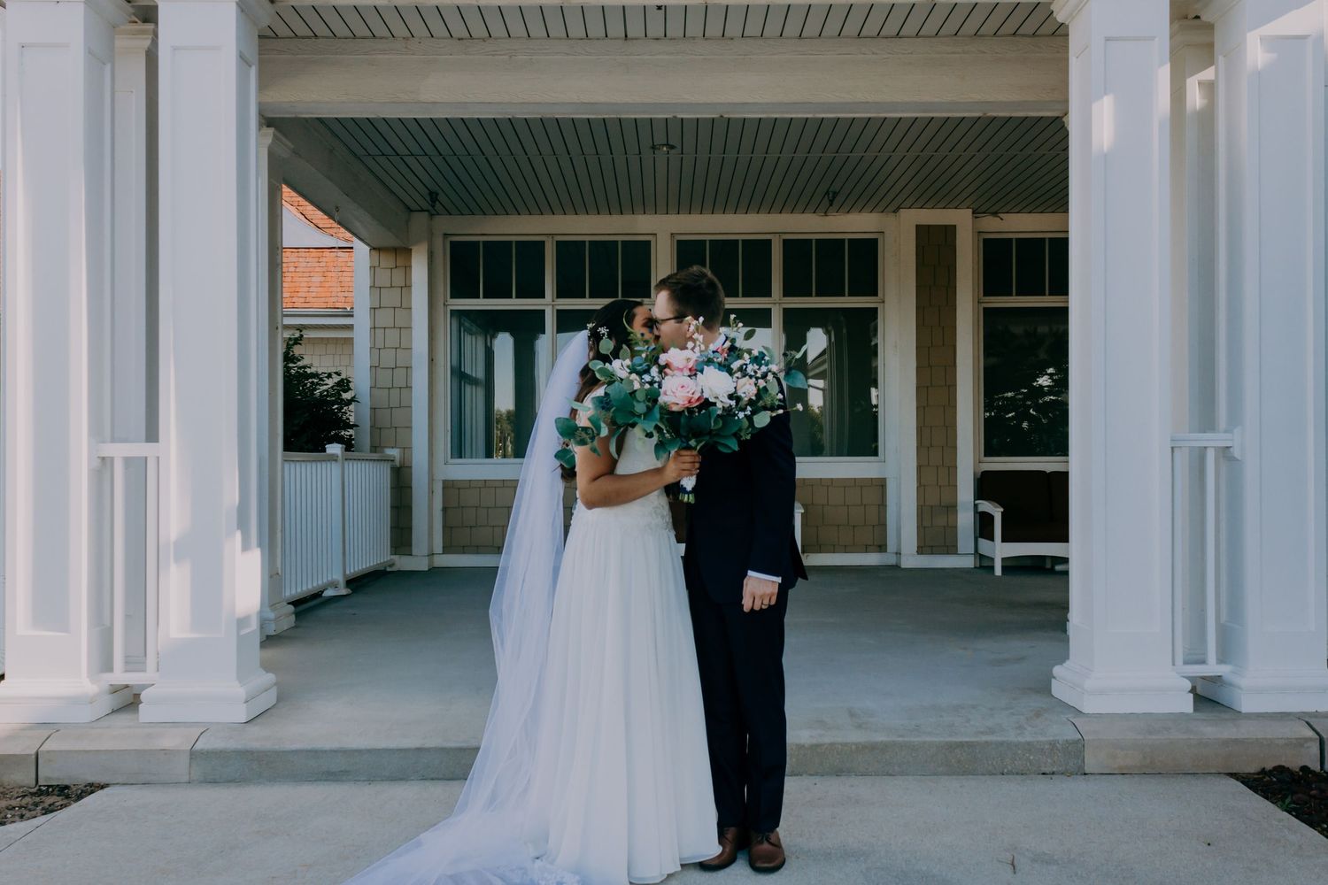 Bride and groom sharing a kiss outside a classic building with white columns on their wedding day.