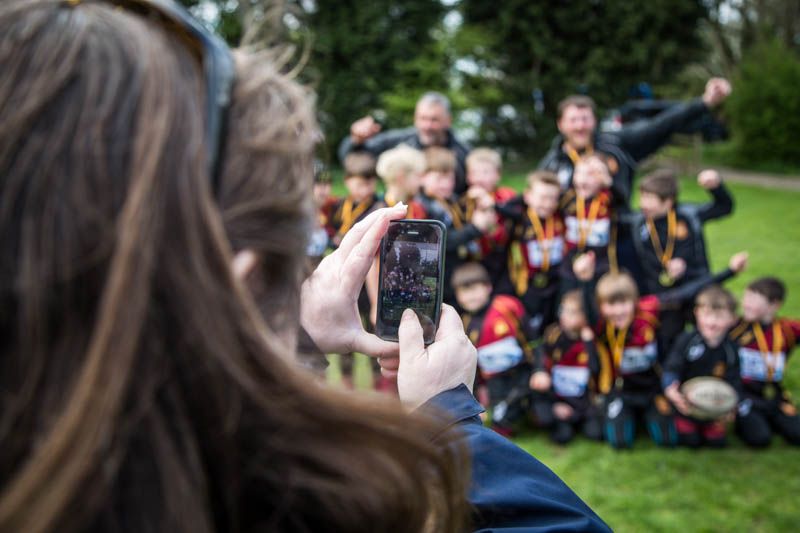 Parent taking photo of youth rugby team celebrating victory during tournament in Gloucestershire