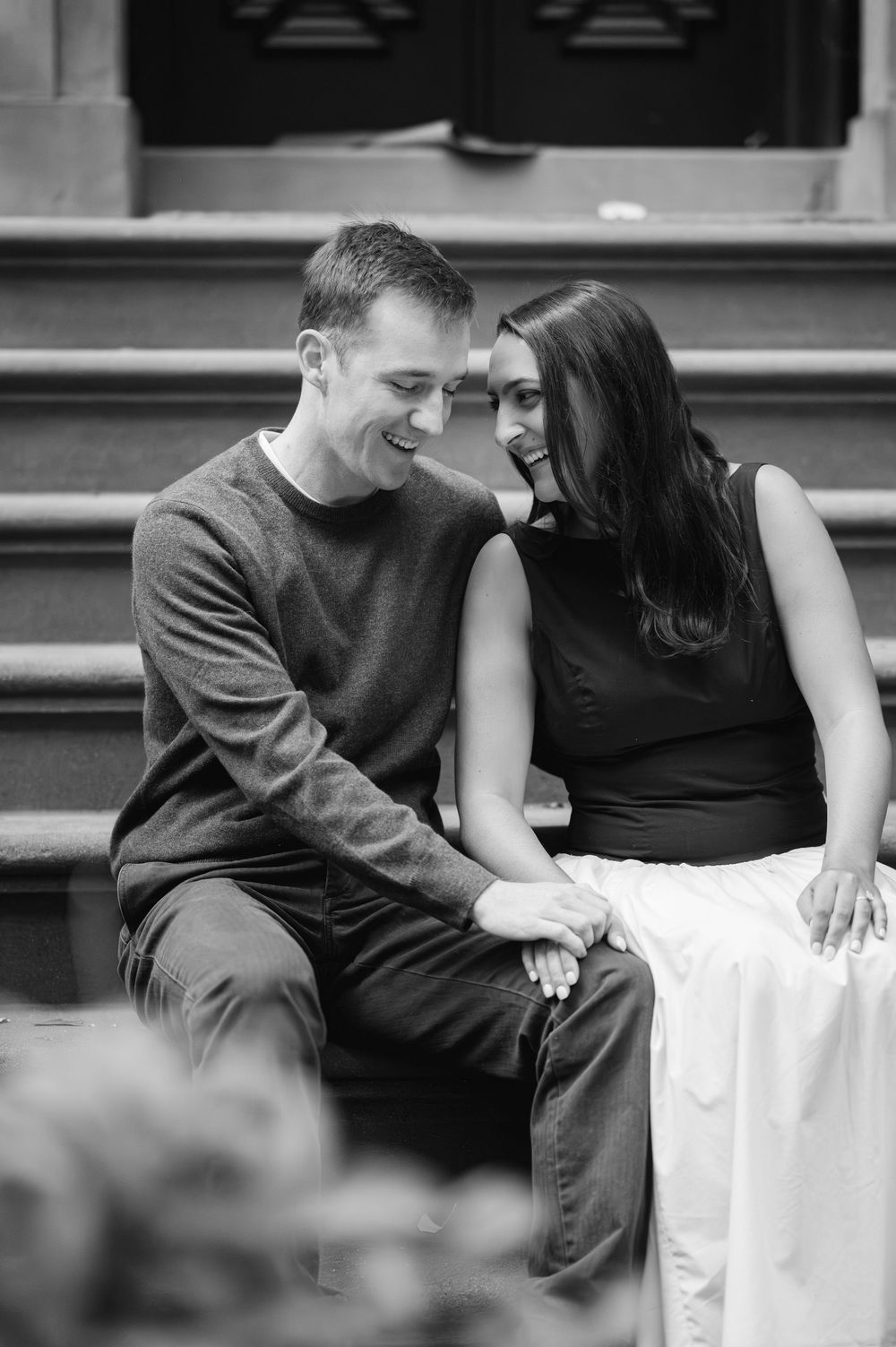 Black and white portrait of a couple sharing intimate moments on brownstone steps.