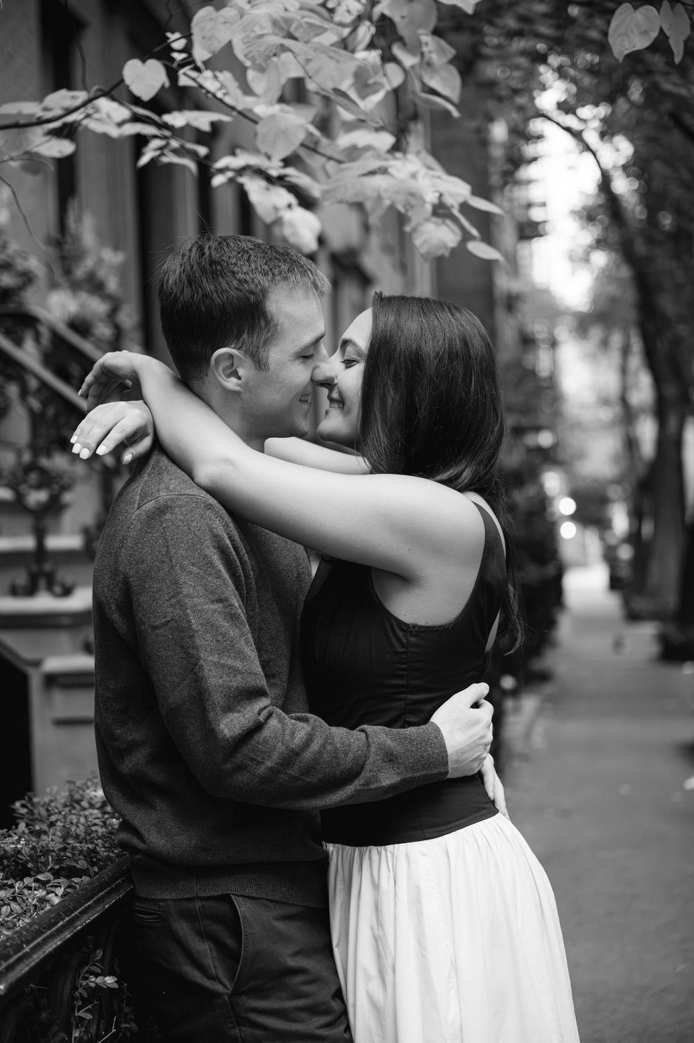 A romantic black and white photograph of a couple embracing on a tree-lined city street.