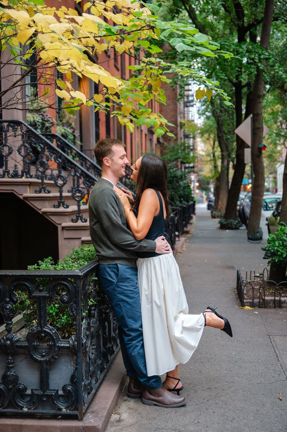 Romantic couple shares tender moments on brownstone steps of tree-lined city street during autumn.