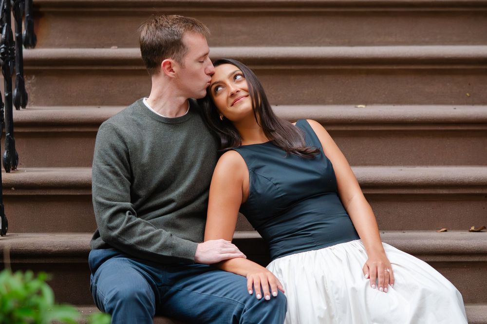 A romantic couple shares tender moments while sitting on brownstone steps during a photoshoot.