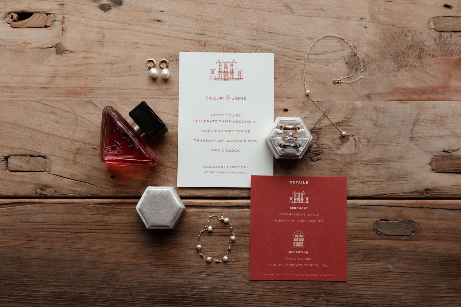 Wedding invitation cards with perfume bottle, watch, and jewelry arranged on rustic wooden surface.