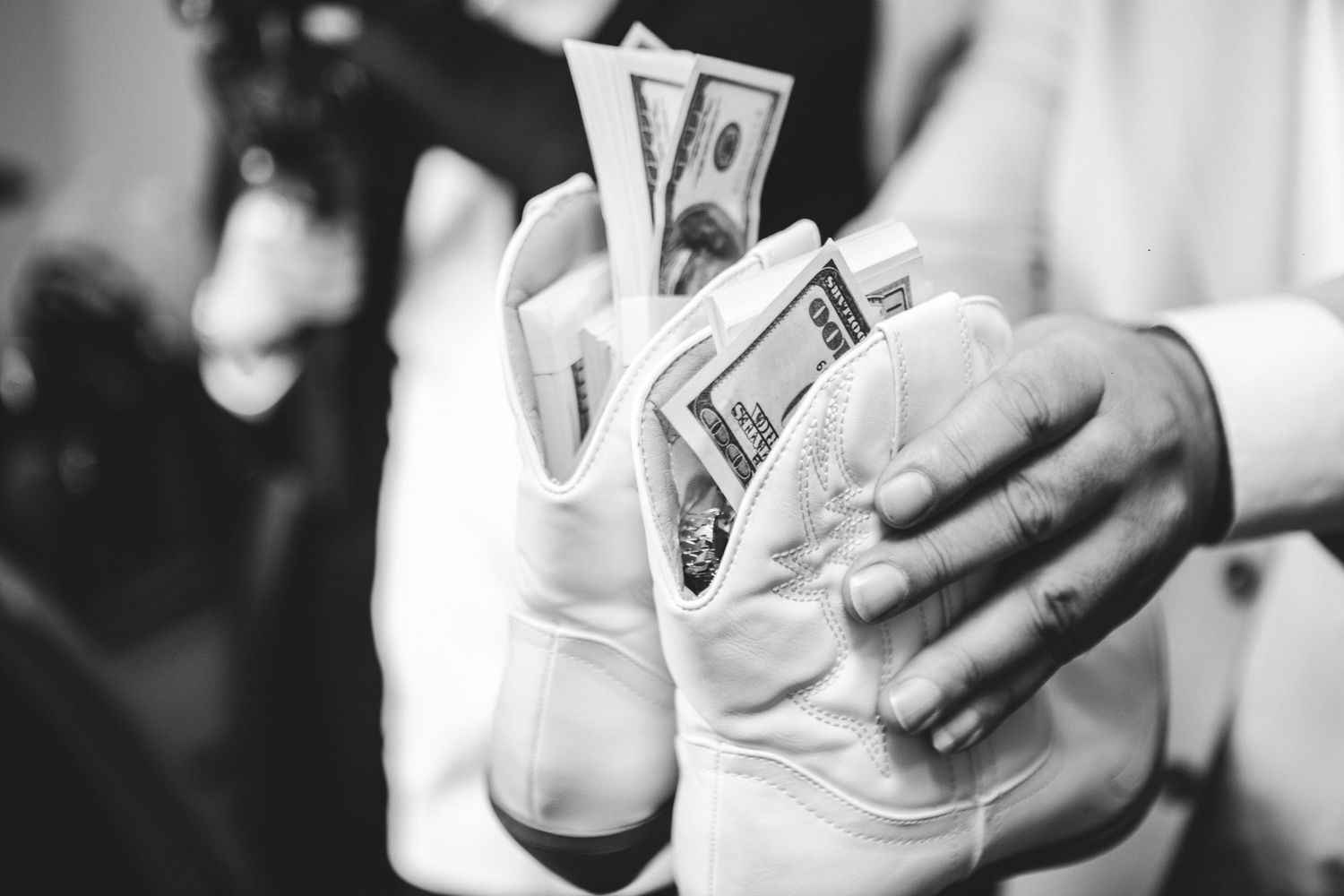Close-up black and white photo of hands placing dollar bills into a white wedding glove.