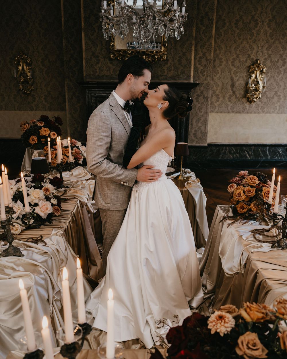 A romantic wedding reception scene with a couple embracing by candlelit tables decorated with flowers and a crystal chandelier.