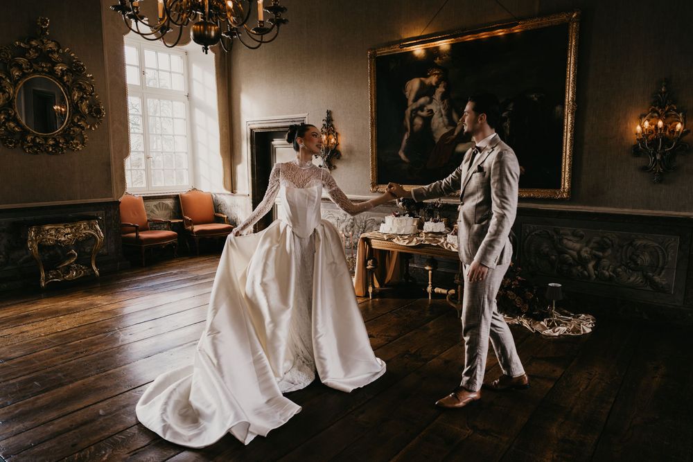 A couple dances together in an elegant ballroom with ornate chandeliers and classic decor.