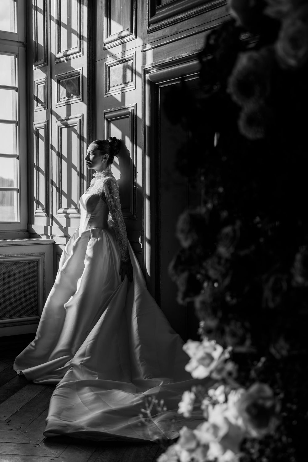 A black and white photo series showing a person in a flowing white dress sitting by sunlit windows.