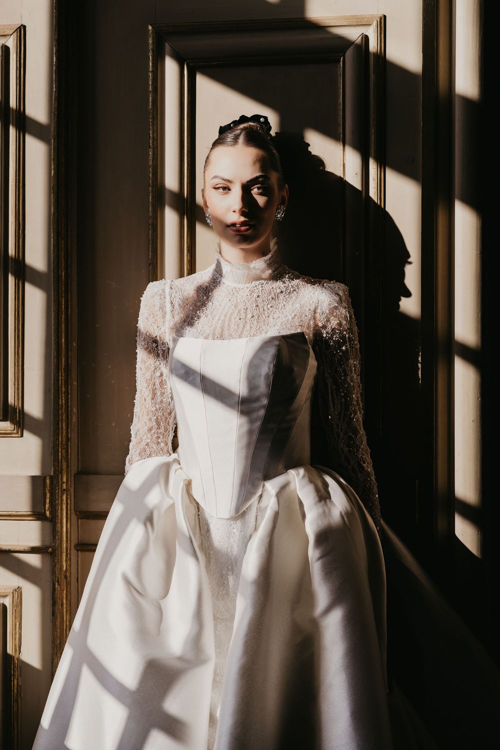 A dramatic bridal portrait with window shadows falling on an elegant white lace and satin wedding gown.