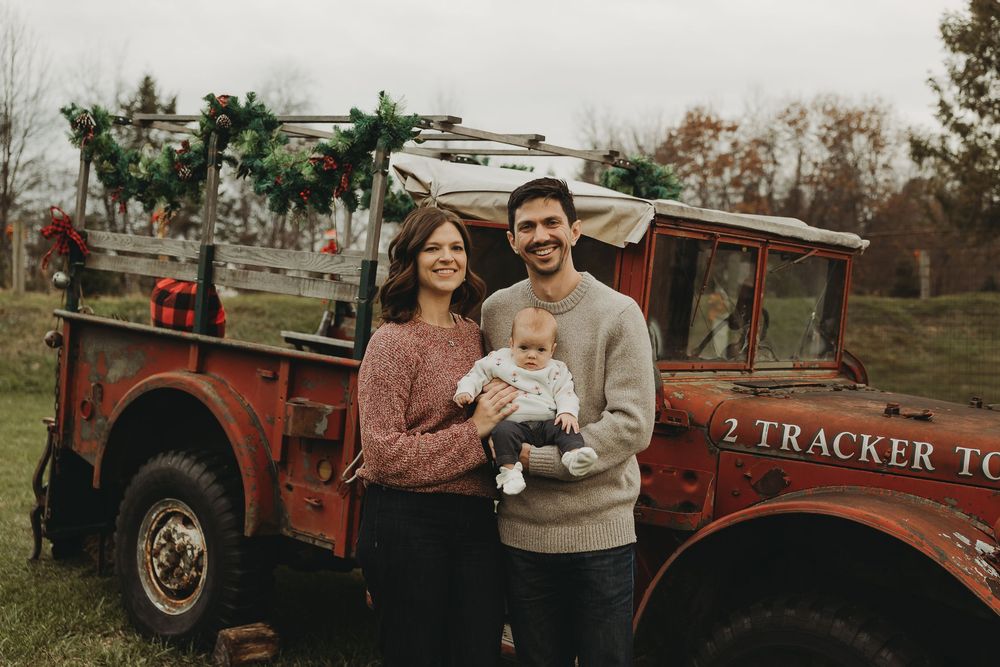 Couple in casual attire poses outdoors near vintage red pickup truck during autumn photoshoot.