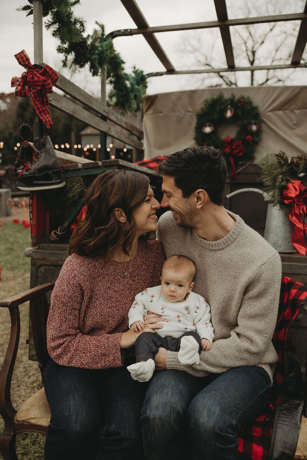 Intimate family moment on decorated holiday bench with baby between parents in cozy sweaters.