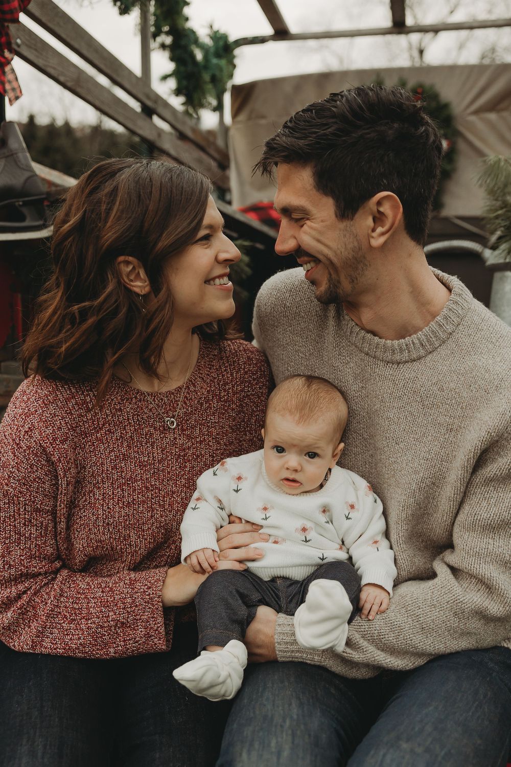 A cozy family moment captured in a series of intimate lifestyle photos showing parents with their baby in warm sweaters.