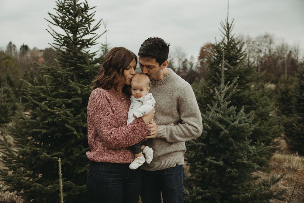 Romantic couple embraces among evergreen Christmas trees at a tree farm on an overcast winter day.