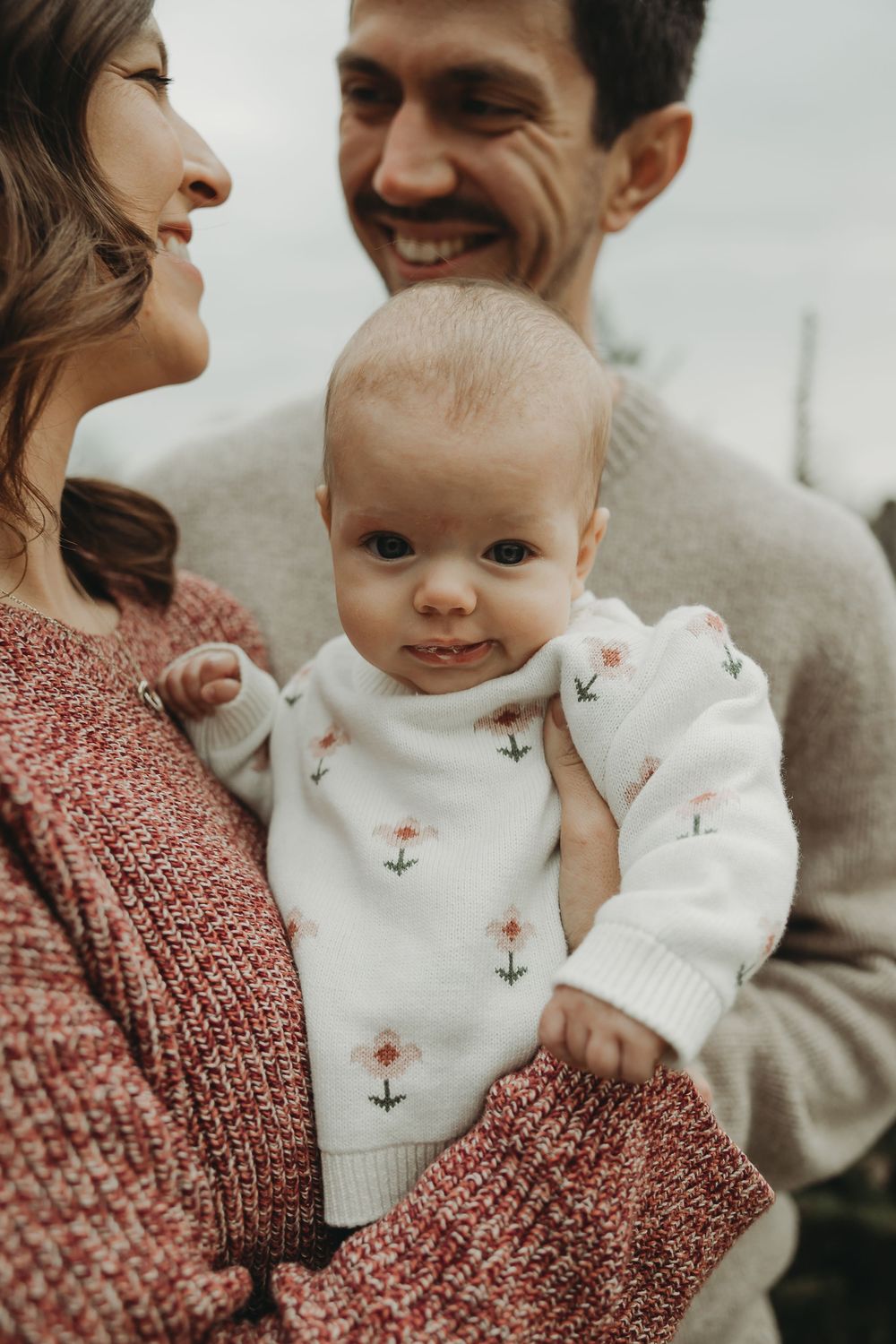 A baby in a white bunny sweater is held lovingly while family members share joyful moments together.